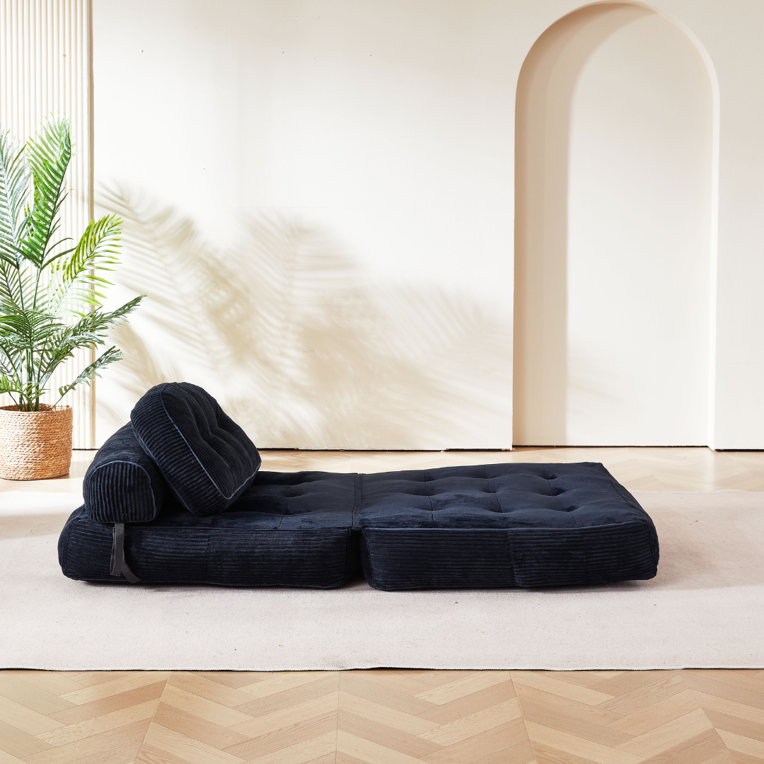 Black cushion on a wooden floor with a plant and archway in the background