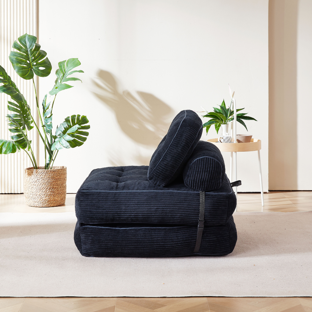 Black corduroy ottoman in a room with plants and a table.